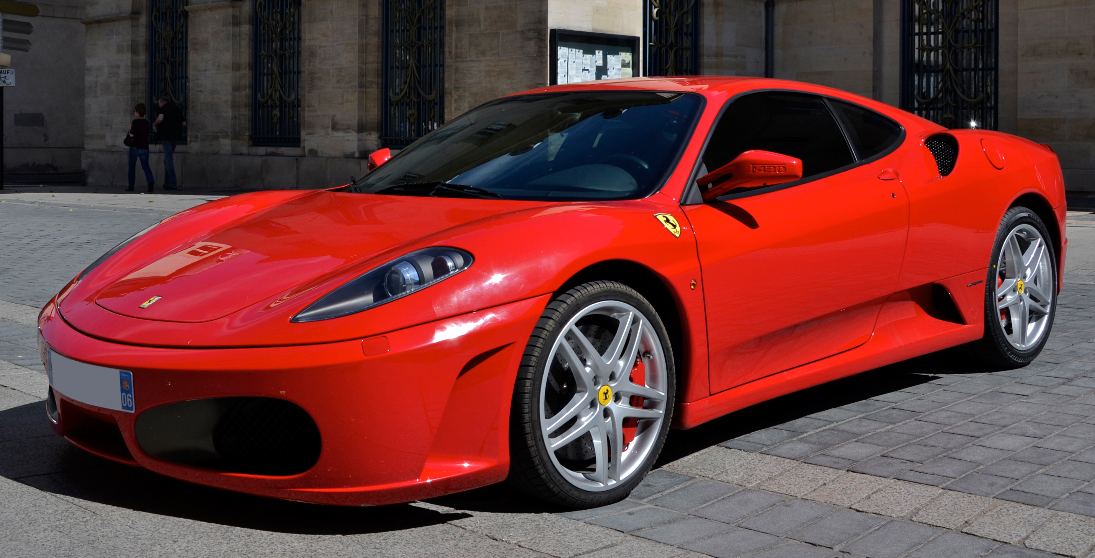 Une Ferrari F430 rouge, garée sur une route panoramique, illustrant son statut de supercar classique prisée.