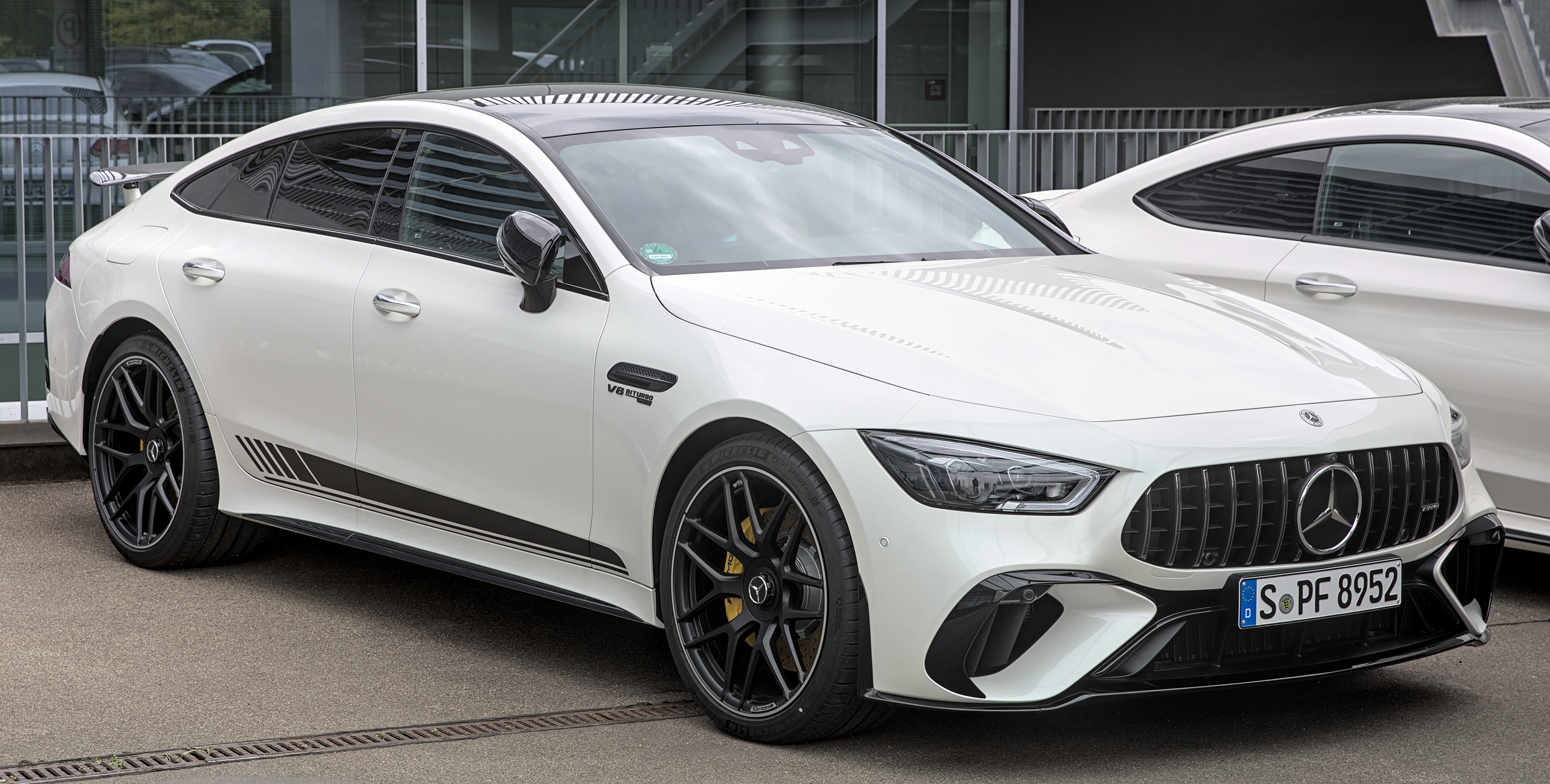 Une Mercedes-AMG GT 63 noire, brillante et sportive, garée devant un bâtiment moderne.