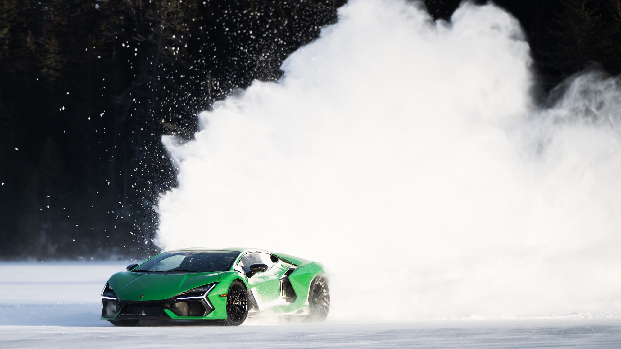 Une Lamborghini Aventador orange, vue de trois quarts avant, roulant sur une route de montagne enneigée et verglacée. La voiture est équipée de pneus hiver et le paysage est hivernal.