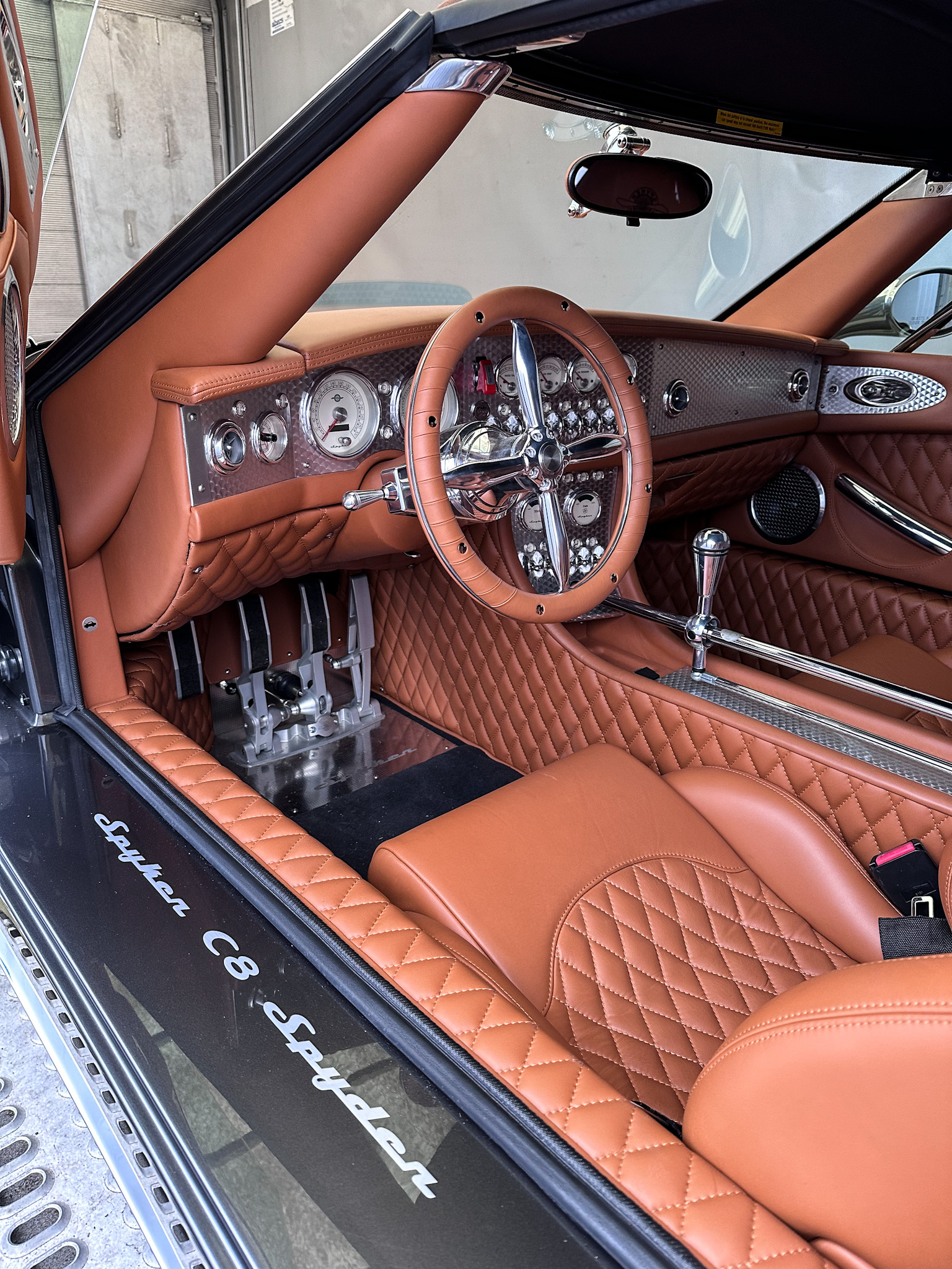 L'intérieur d'une Spyker C8, montrant le tableau de bord détaillé avec des cadrans ronds, le volant sport et les sièges en cuir marron.