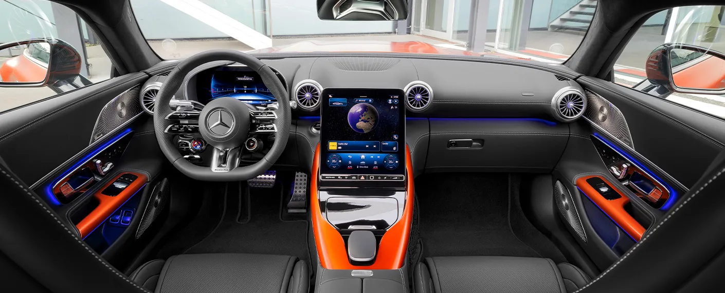 Intérieur d'un Mercedes-AMG GT Coupé 4 Portes 2025, montrant le tableau de bord numérique et l'écran central MBUX affichant des informations de navigation, avec des sièges en cuir noir et des accents de fibre de carbone.