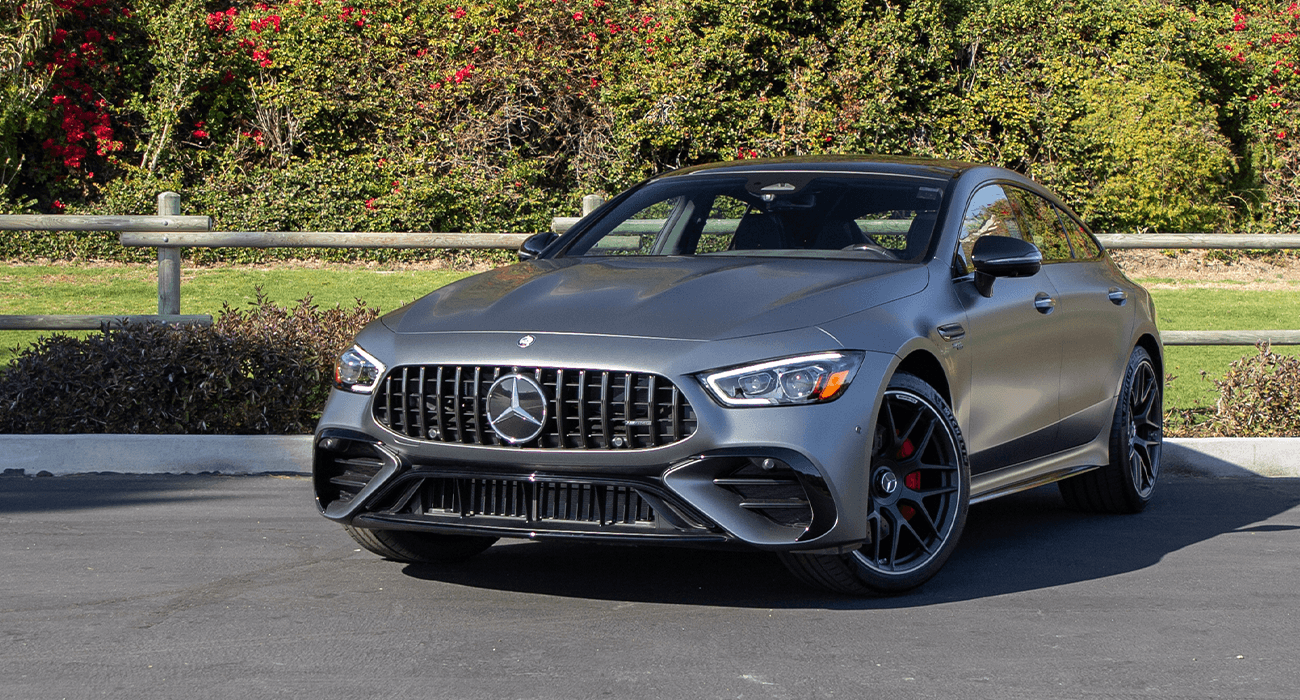 Vue latérale d'un Mercedes-AMG GT Coupé 4 Portes 2025 gris foncé en mouvement sur une route de campagne, mettant en valeur son design élégant et ses jantes sportives.