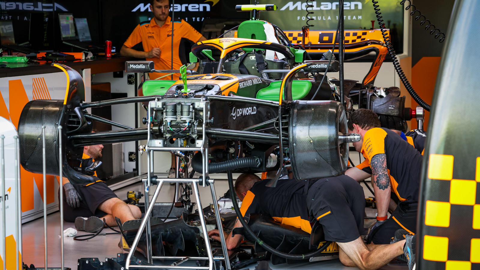 Des ingénieurs de l'équipe McLaren F1 travaillant avec concentration sur une voiture de course dans un garage, installant de nouvelles pièces.