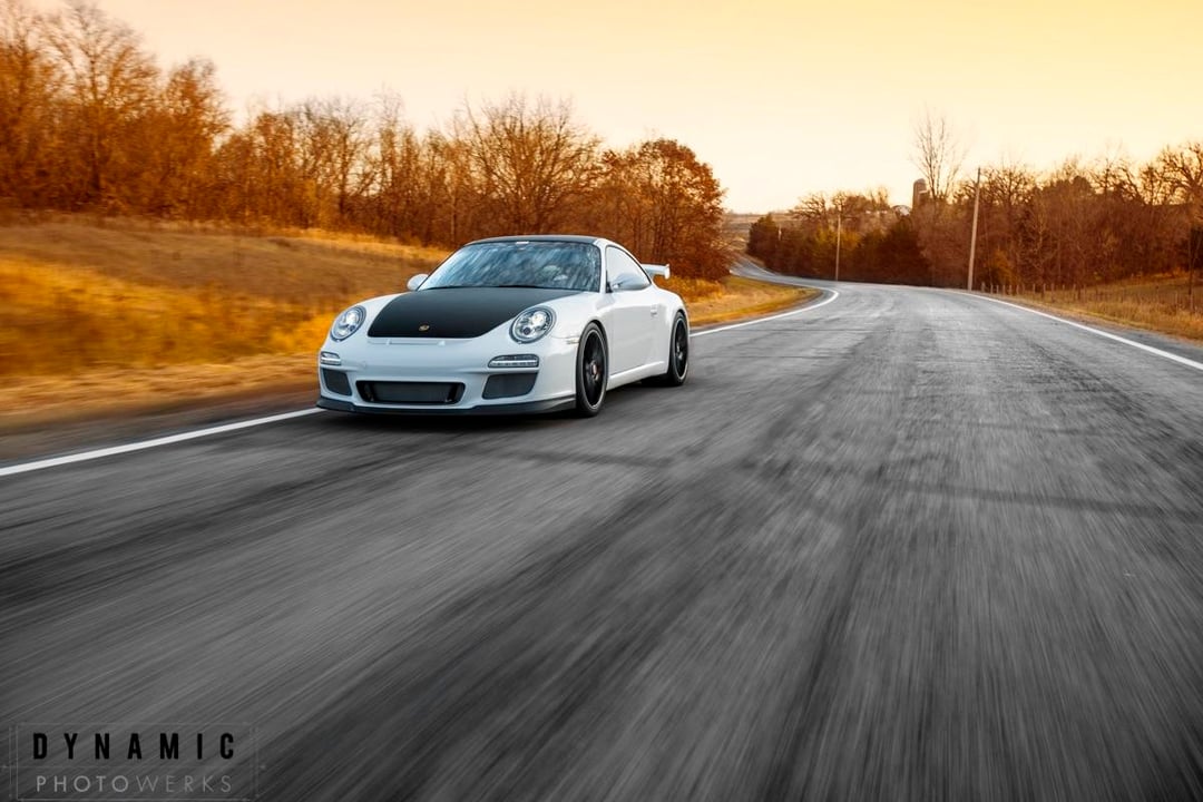 Une Porsche 997.2 GT3 blanche en pleine accélération sur un circuit de course, vue de côté.