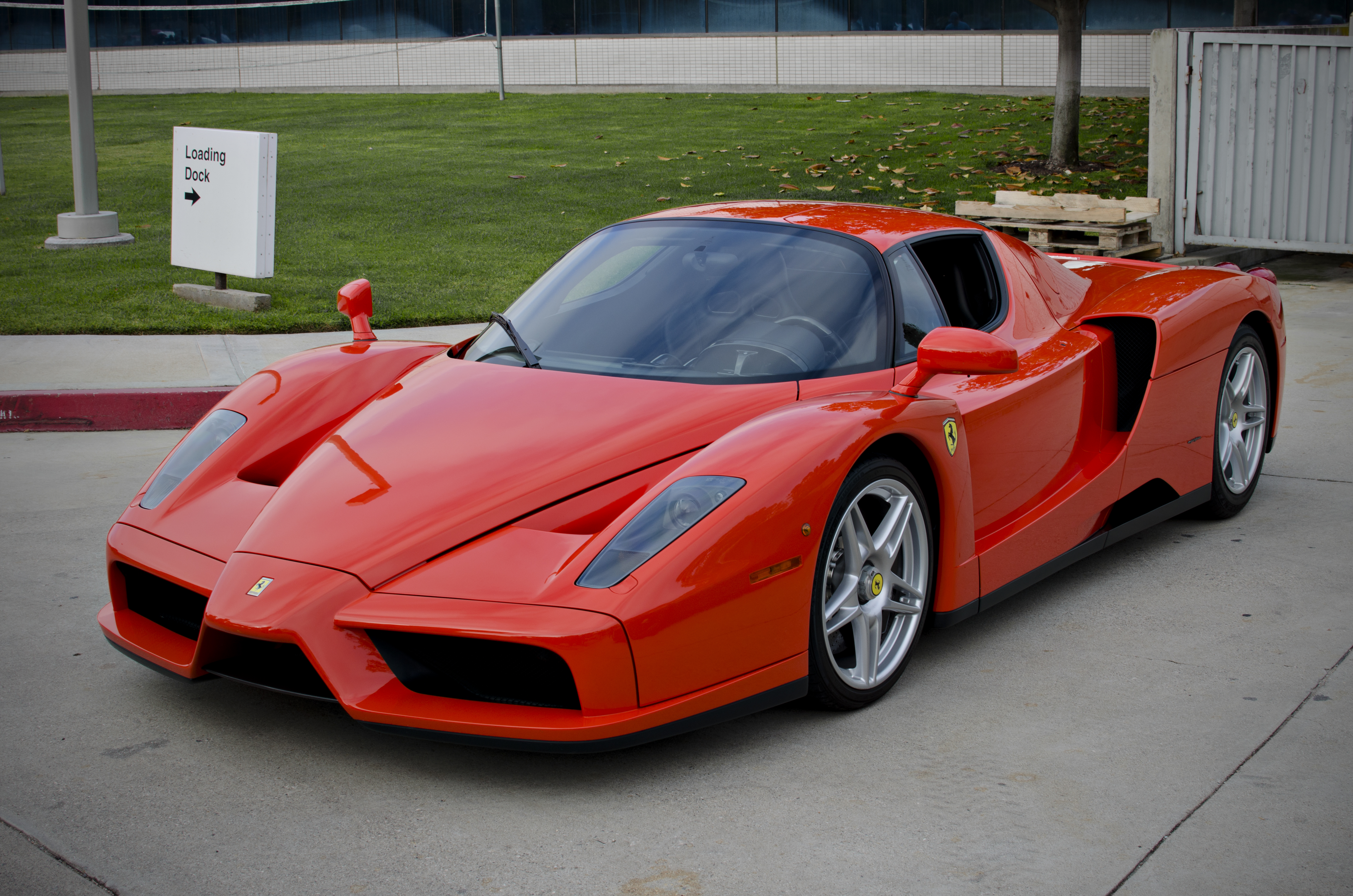 Une Ferrari Enzo rouge, vue de trois quarts arrière, mettant en évidence son moteur V12 central visible à travers la lunette arrière.