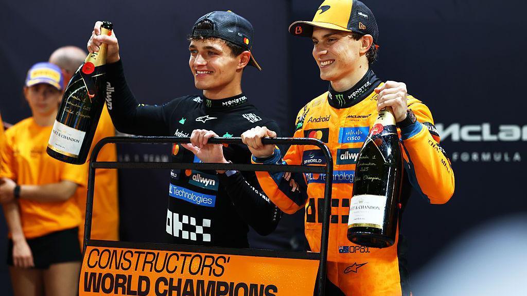 Oscar Piastri et Lando Norris posant ensemble devant une voiture McLaren de Formule 1, illustrant la cohésion de l'équipe.