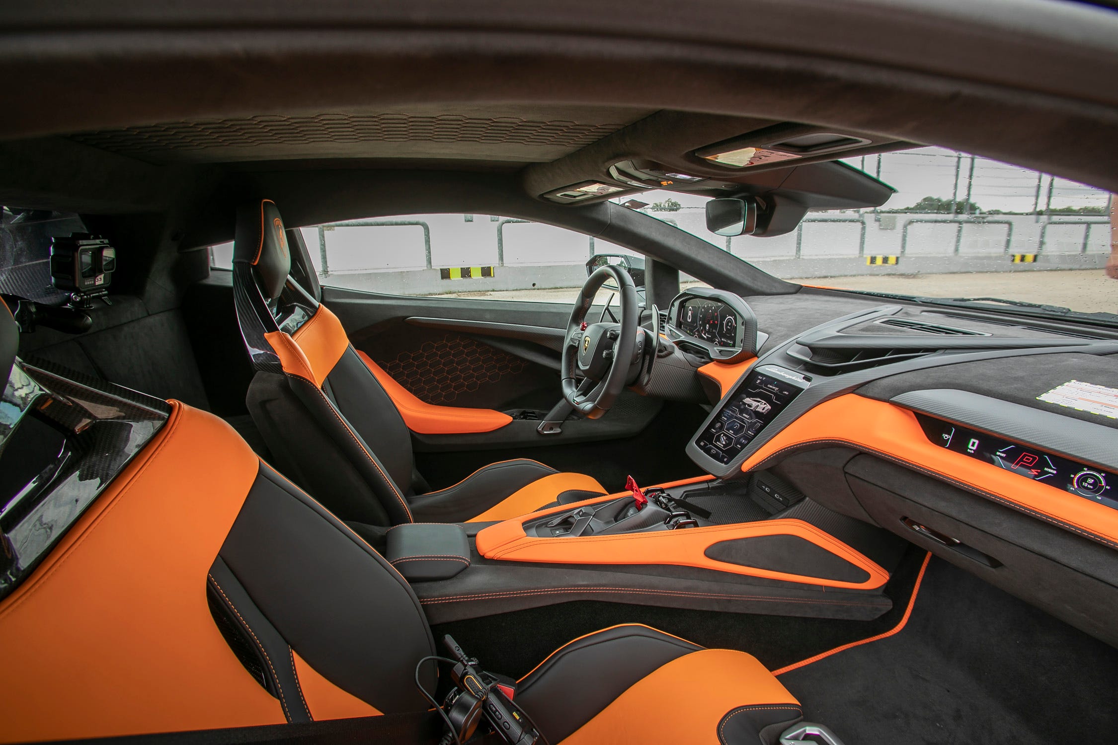 Intérieur du cockpit d'une Lamborghini Revuelto 2024, montrant le volant, le tableau de bord numérique et les sièges sport en Alcantara noir avec des détails rouges.