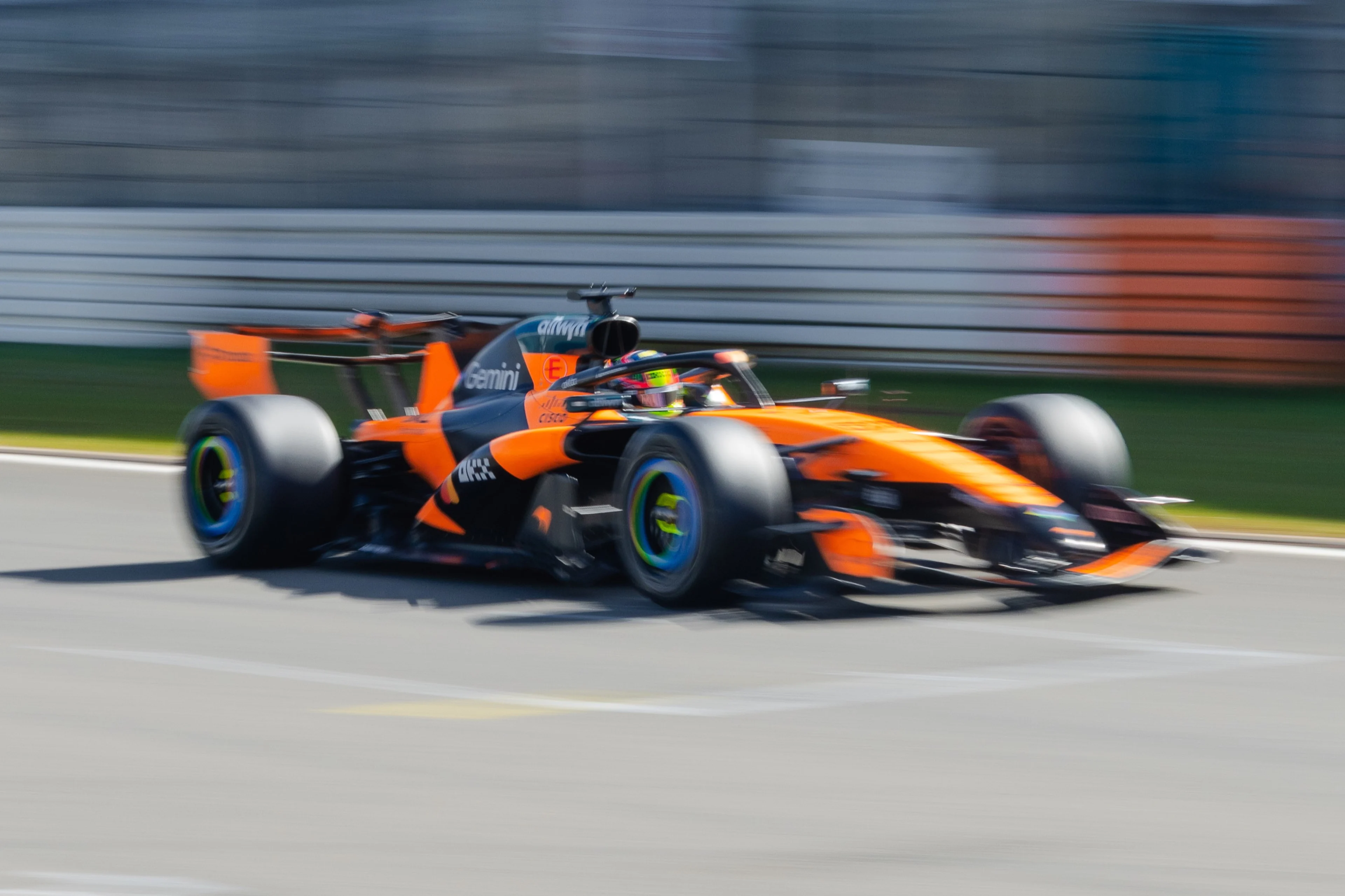 Une McLaren de Formule 1 orange et noire roule sur le Nürburgring sous la pluie, avec des pneus Pirelli visibles, lors d'une séance d'essais.