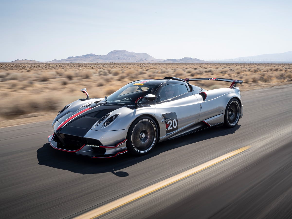 Une Pagani Huayra BC rouge et noire, portes ouvertes, exposant son intérieur détaillé et ses éléments aérodynamiques sur une piste de course.