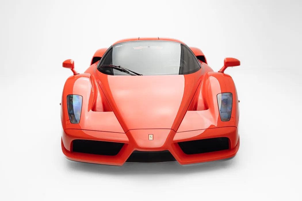 Une Ferrari Enzo rouge, vue de trois quarts avant, mettant en valeur ses lignes aérodynamiques et son allure sportive.