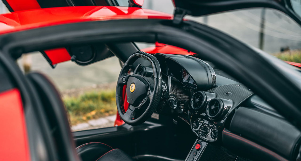 L'habitacle d'une Ferrari Enzo, présentant des sièges en Alcantara rouge et noir et des conduits d'aération spécifiques.