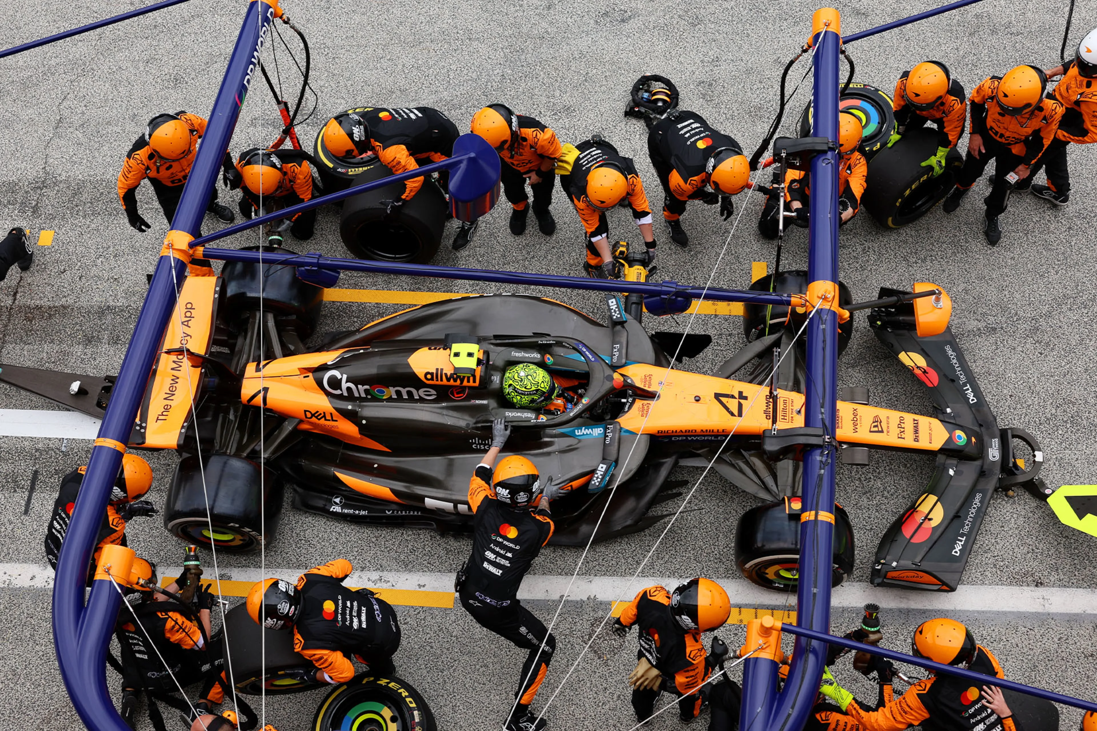 Image d'un arrêt au stand d'une McLaren de Formule 1, avec l'équipe de mécaniciens changeant les pneus à grande vitesse, illustrant l'efficacité opérationnelle.