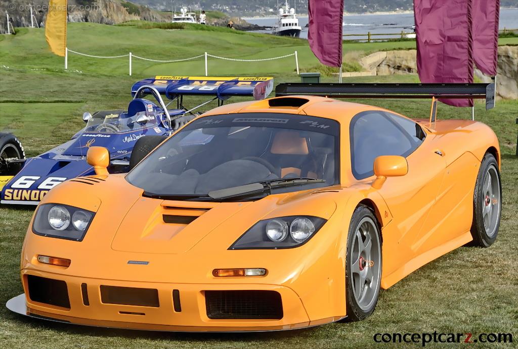 Une McLaren F1 orange vif de 1995, garée dans les rues de Monaco, avec des bâtiments élégants en arrière-plan.