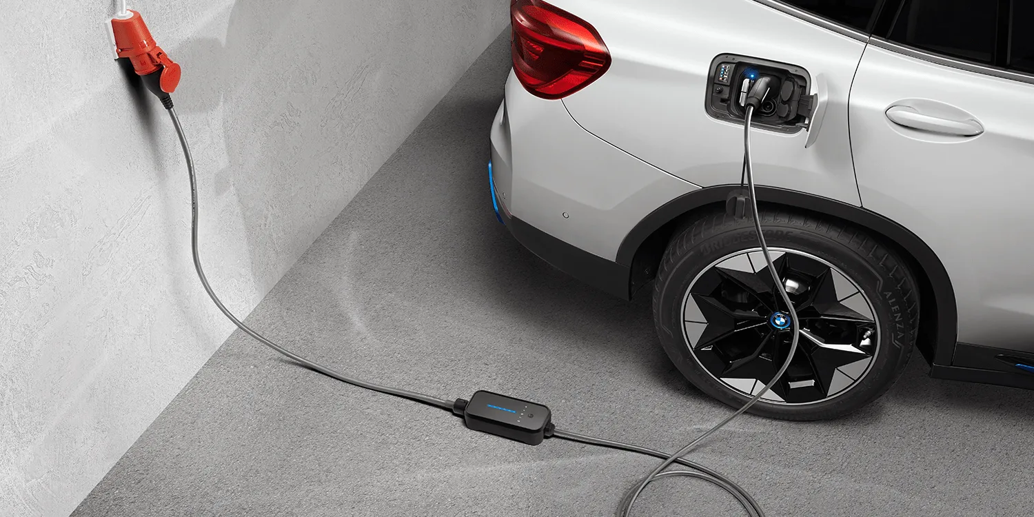 Un SUV électrique BMW iX3 blanc branché à une station de recharge rapide dans un environnement urbain chinois.