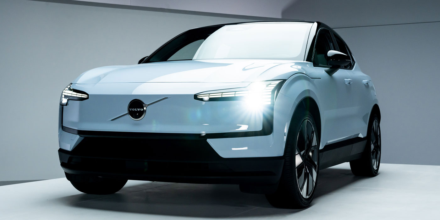 Une Volvo EX30 2026 blanche est branchée à une borne de recharge dans un environnement urbain moderne au crépuscule.