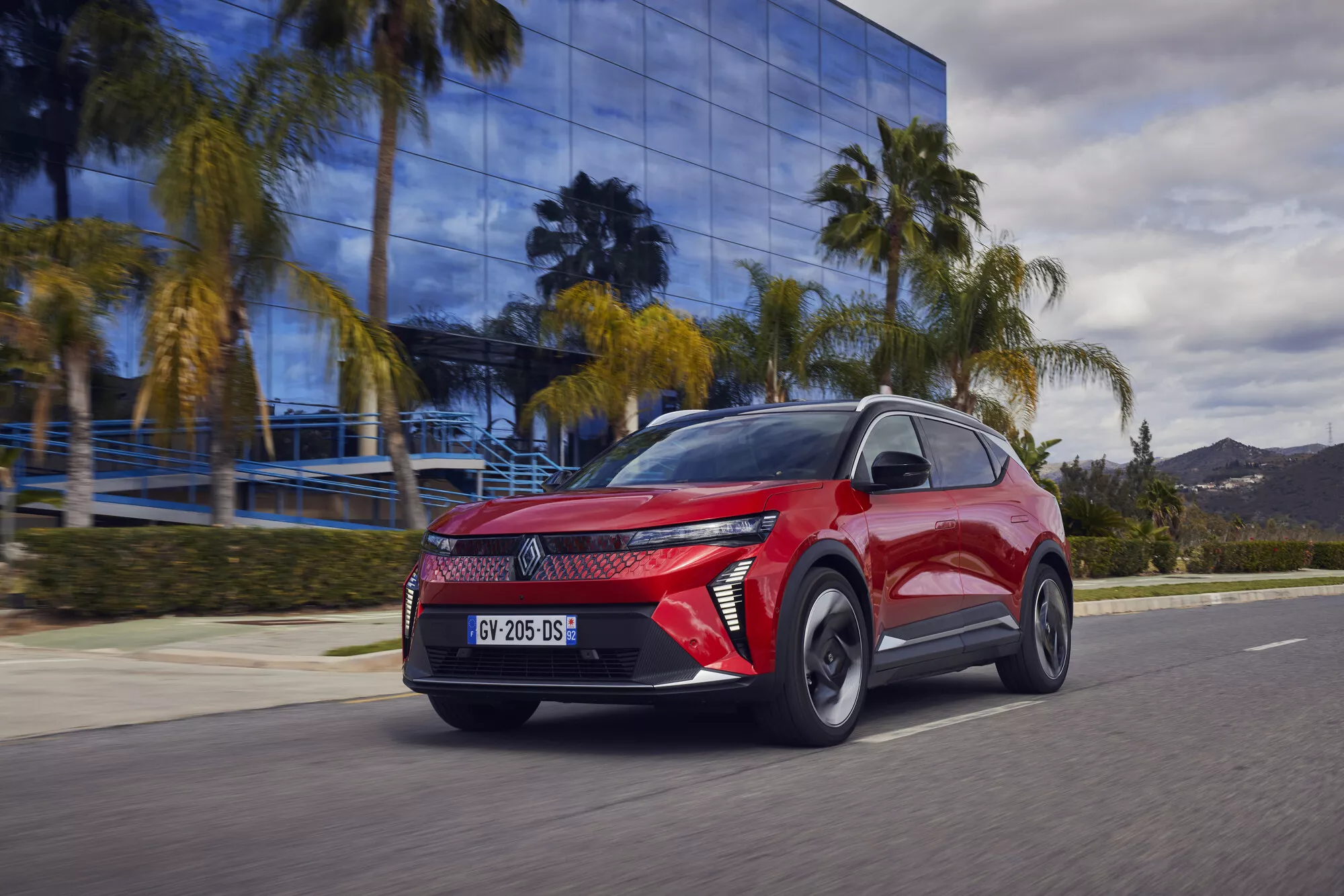 Un Renault Scénic E-Tech 100% électrique de couleur claire roule sur une route de campagne française ensoleillée.