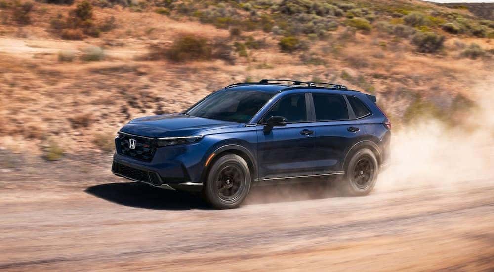 Une Honda CR-V hybride de couleur moderne roulant sur une route de campagne avec des collines verdoyantes en arrière-plan.