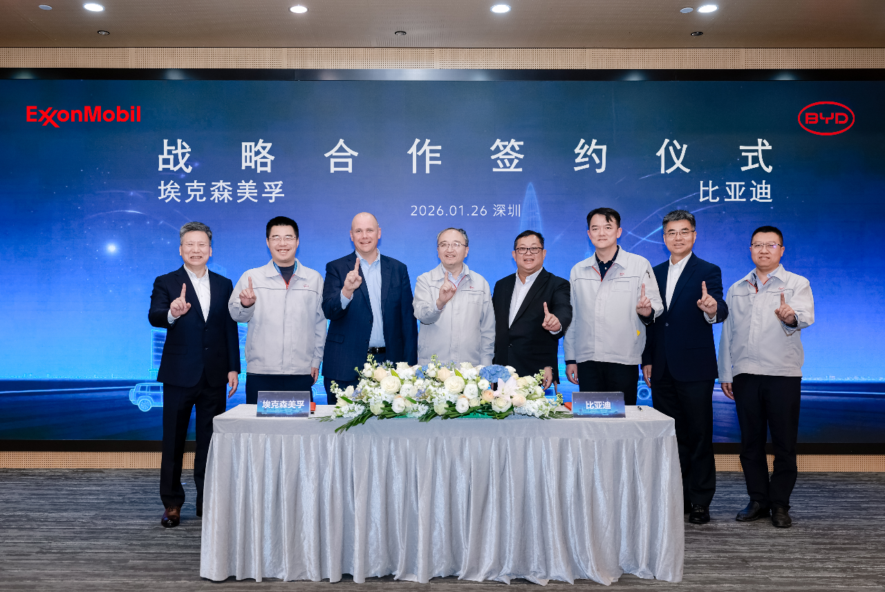 Deux dirigeants, l'un de BYD et l'autre d'ExxonMobil, se serrent la main devant un panneau affichant les logos des deux entreprises, symbolisant la signature d'un accord.