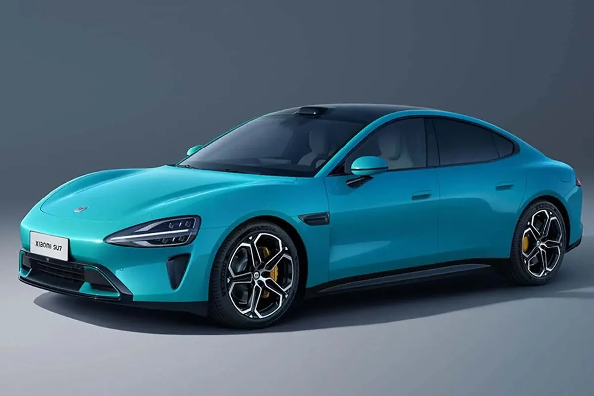 Une voiture électrique Xiaomi SU7 de couleur vive, roulant dans une ville illuminée au crépuscule.