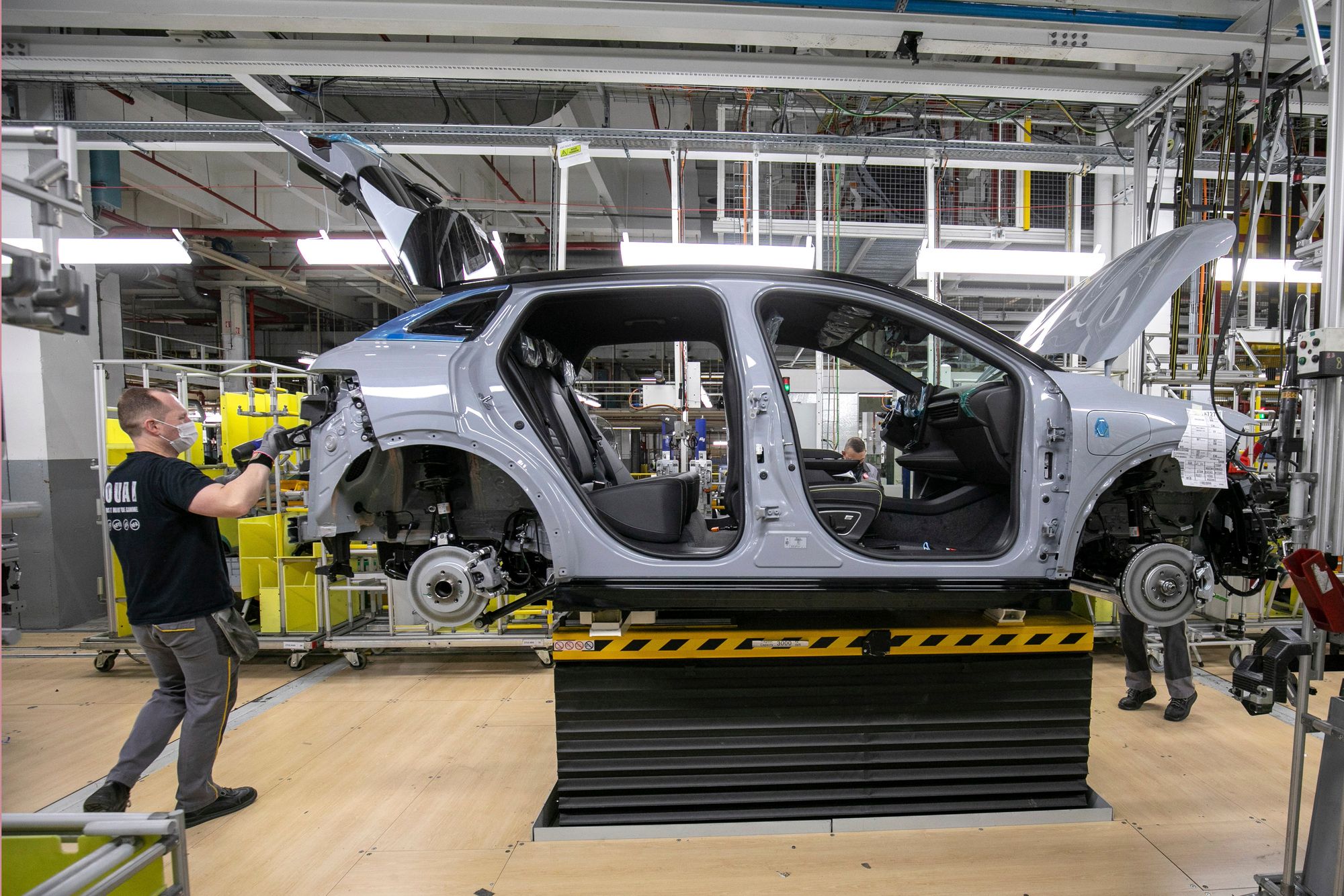Ligne d'assemblage d'une usine française de voitures électriques, avec des robots et des ouvriers.