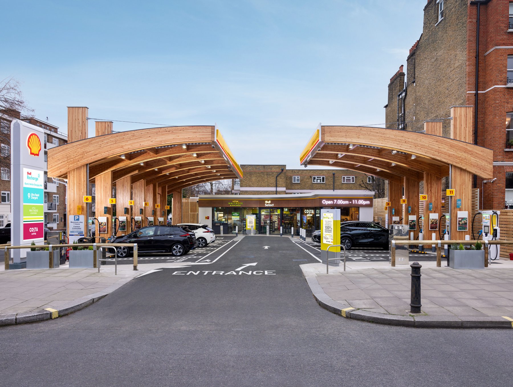 Une station de recharge moderne pour véhicules électriques en Europe, avec plusieurs voitures électriques, dont des modèles Nio, en train de charger ou en attente. L'environnement est urbain et contemporain.