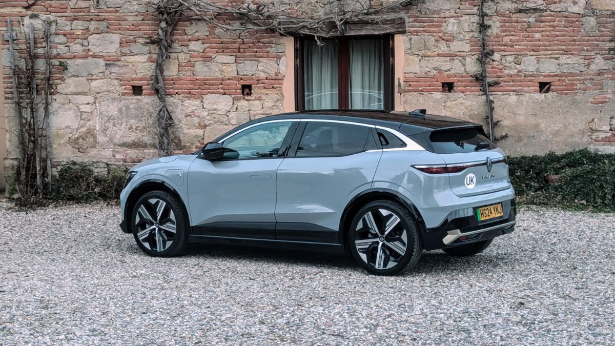 Une Renault Mégane E-Tech blanche en mouvement sur une route de campagne française, avec des vignobles en arrière-plan.