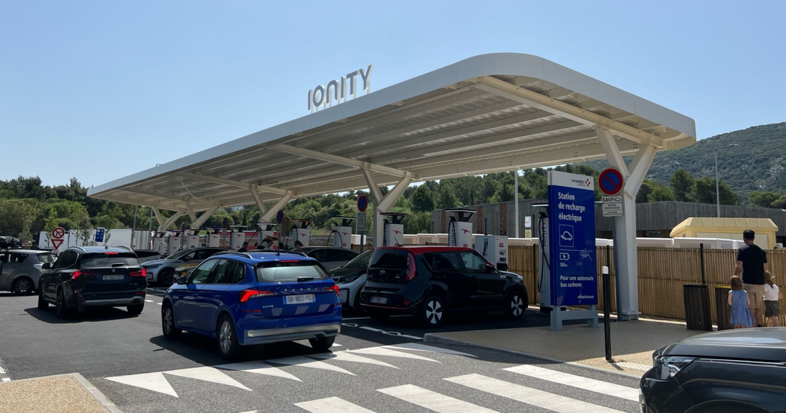 Une longue file de voitures électriques attendant de recharger à une station bondée pendant un week-end de vacances.