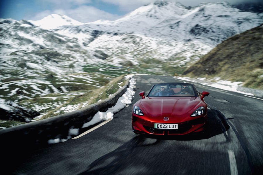 Le MG Cyberster, un roadster électrique, roulant sur une route de campagne européenne avec des virages. La voiture est en mouvement, suggérant une conduite sportive.