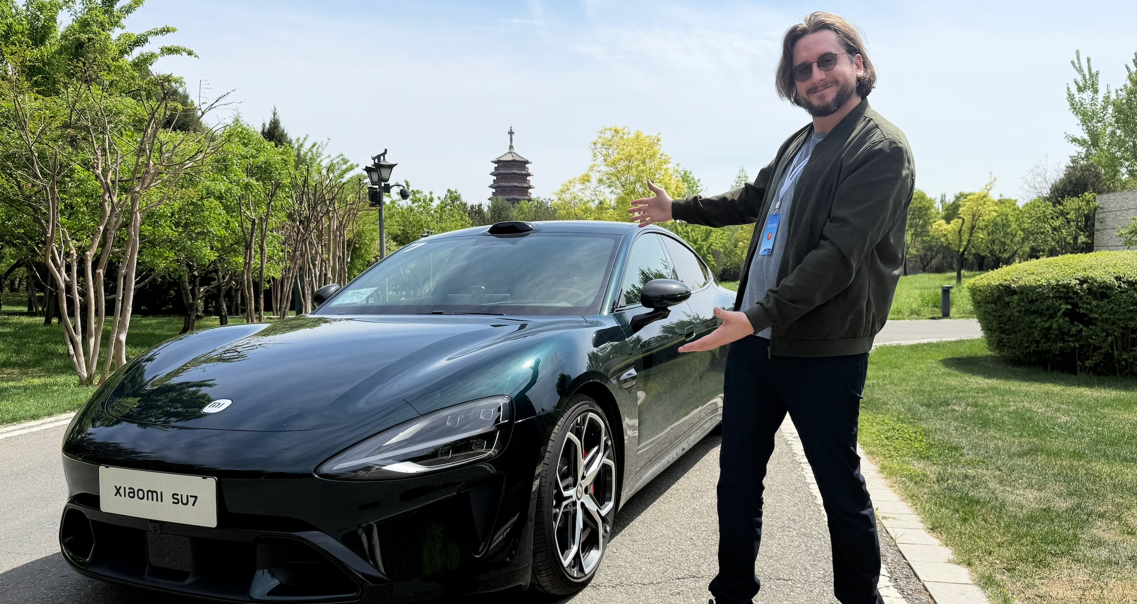 Une voiture électrique Xiaomi SU7 de couleur vive roulant sur une route de campagne, avec un paysage en arrière-plan.