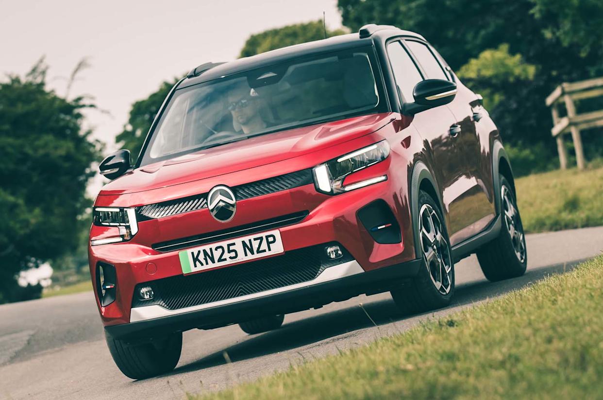 Une Citroën ë-C3 électrique de couleur vive roulant sur une route de campagne, avec des champs et des collines en arrière-plan.