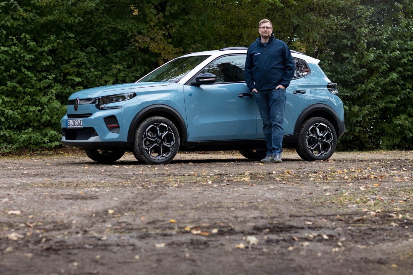 Une Citroën ë-C3 électrique de couleur vive roulant sur une route de campagne, avec des champs et des collines en arrière-plan.