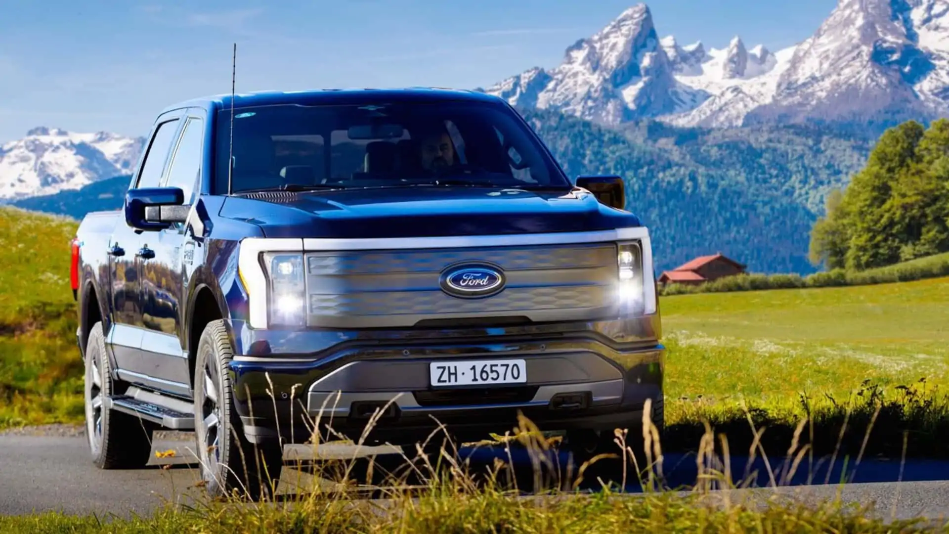 Un Ford F-150 Lightning blanc circulant dans une rue étroite d'une ville européenne, avec des bâtiments anciens en arrière-plan.