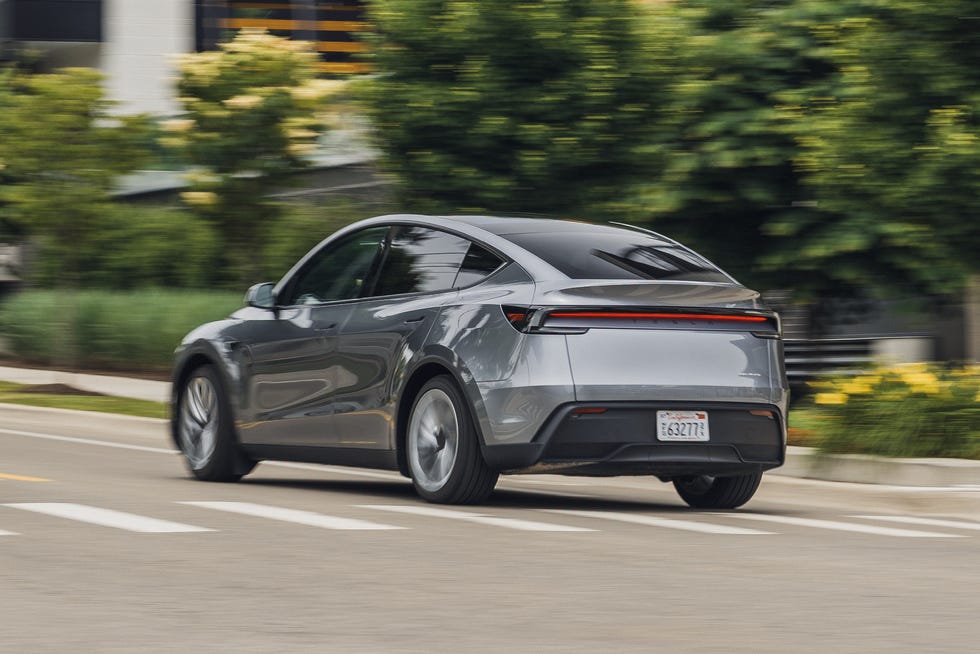 Une Tesla Model Y 2026 blanche roulant sur une autoroute, avec un paysage montagneux en arrière-plan.