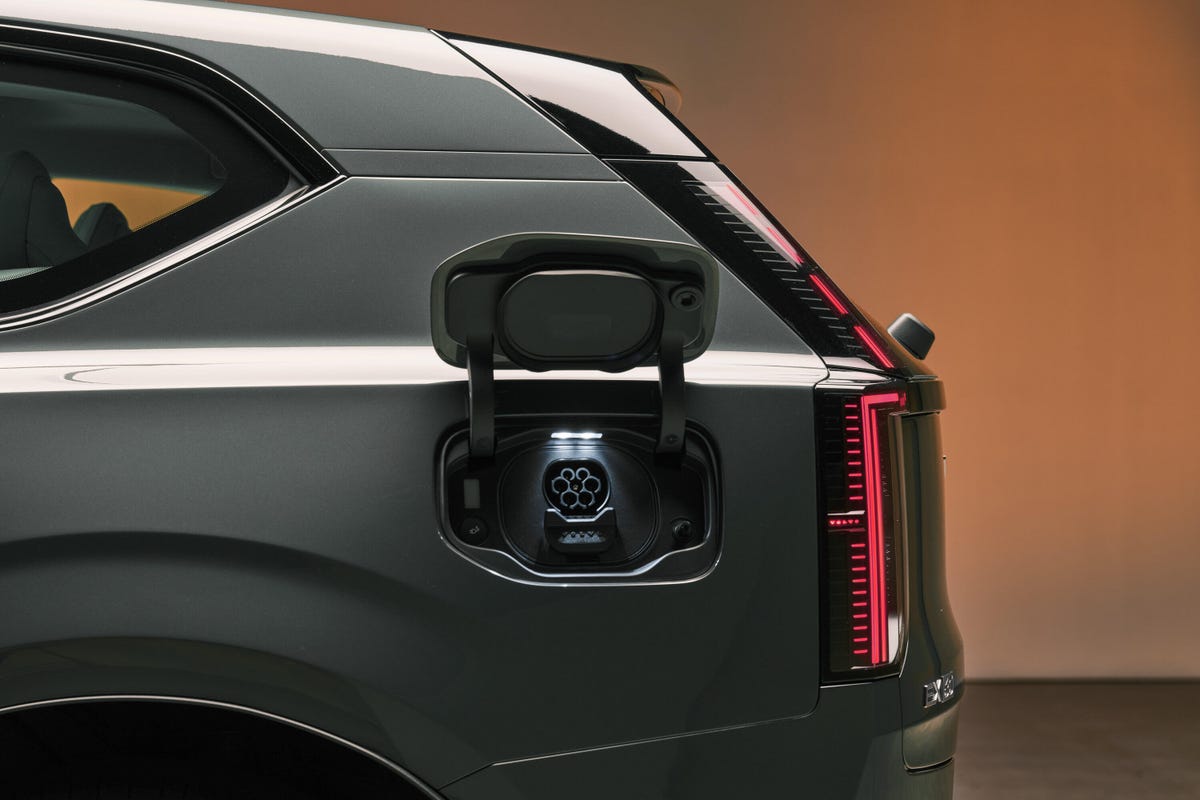 Une Volvo EX60 électrique de 2026 en train de charger à une borne rapide, avec des lumières urbaines en arrière-plan.