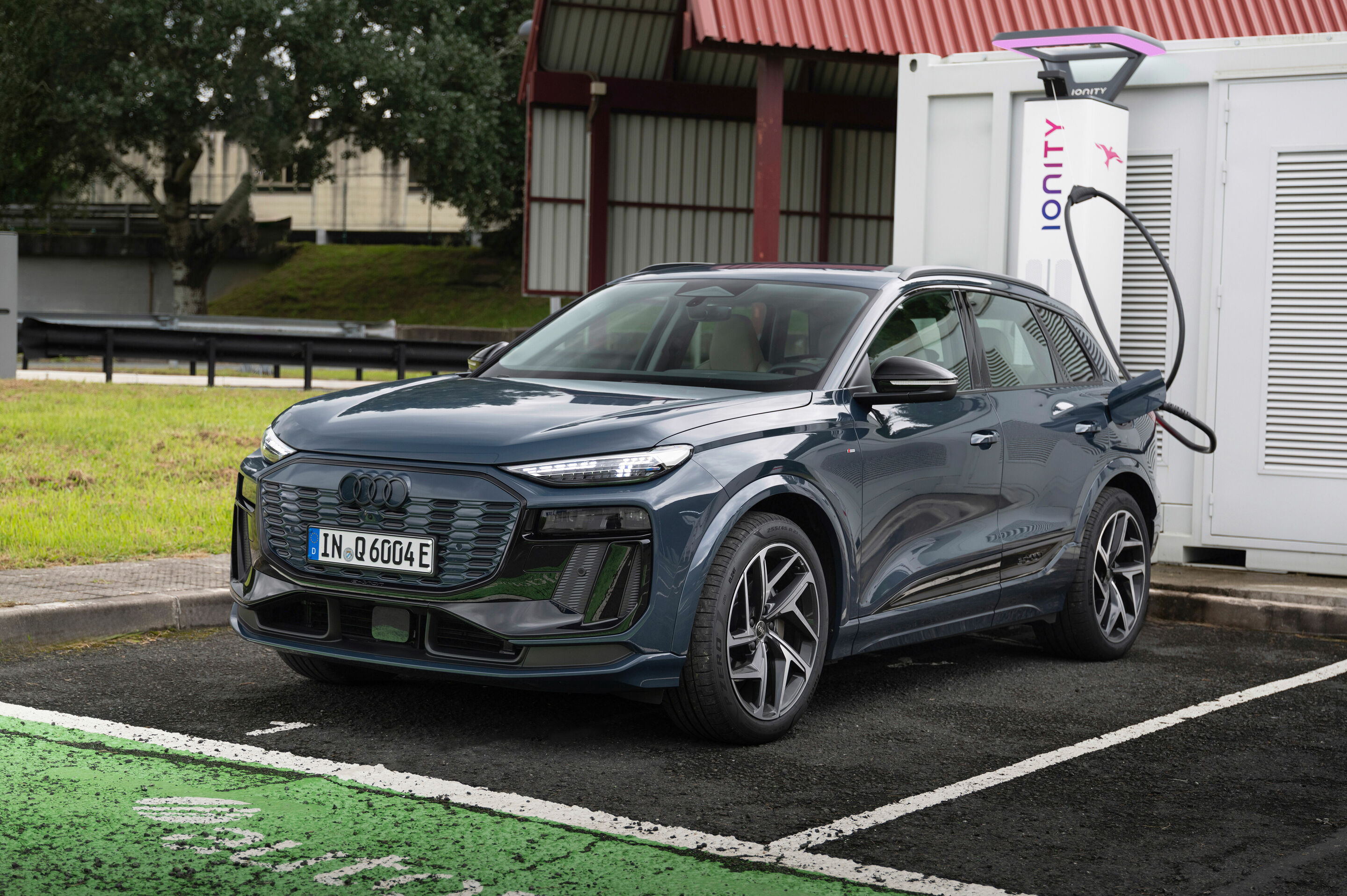 Une Audi Q6 e-tron 2027 branchée à une borne de recharge rapide, vue de côté.
