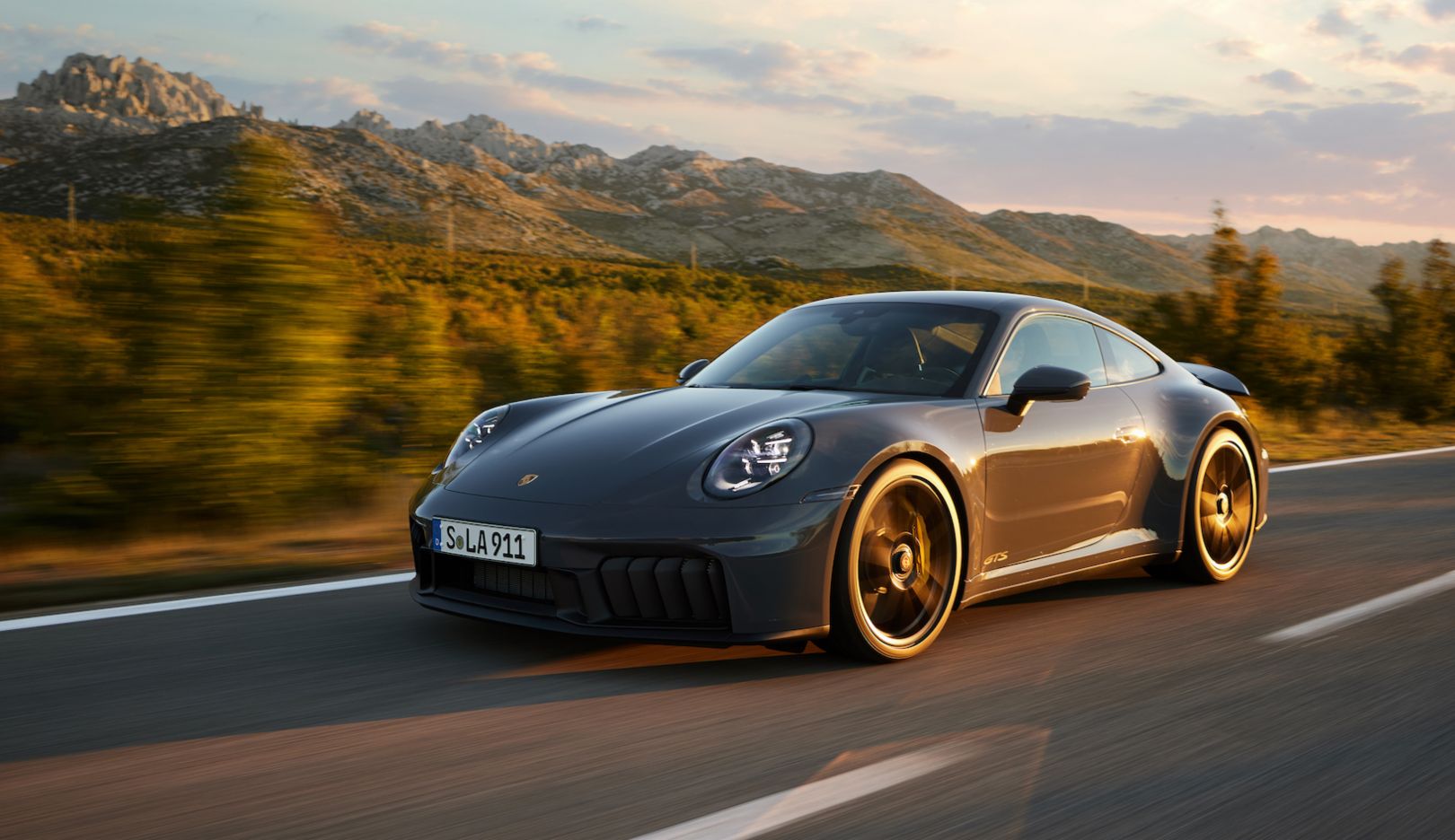 Une Porsche 911 hybride de couleur vive roulant sur une route de montagne sinueuse.