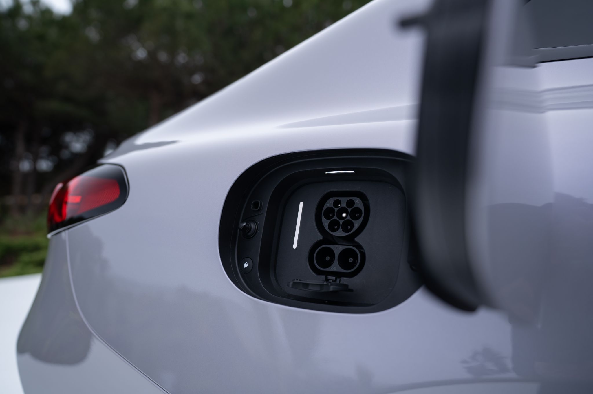 Gros plan sur le port de recharge d'une Mercedes Classe C électrique, avec un câble branché, et un aperçu du tableau de bord affichant l'autonomie.