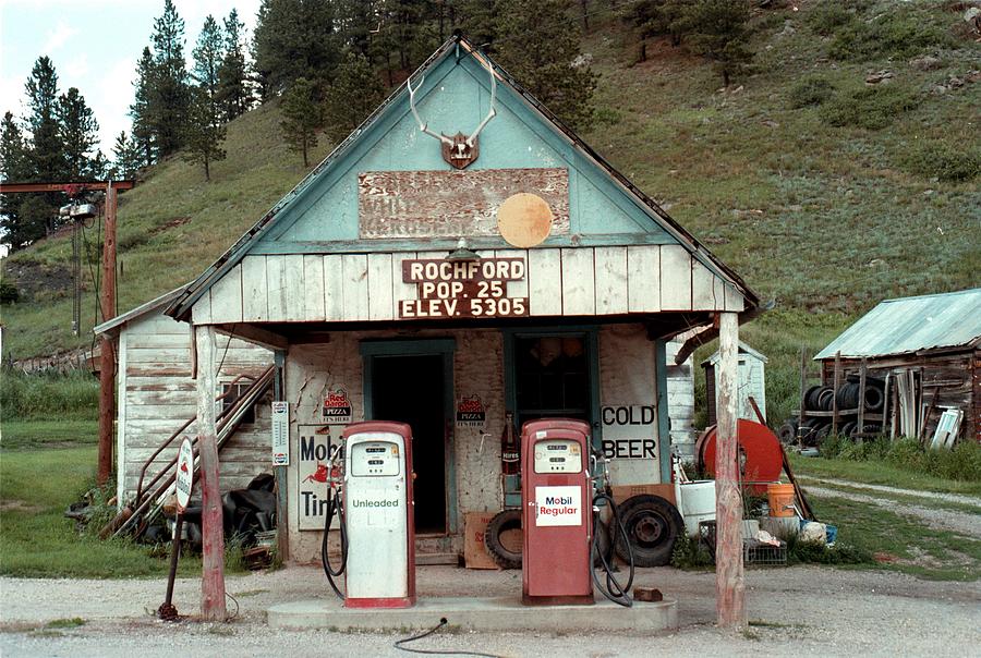 Photographie d'une station-service isolée en milieu rural, avec des pompes à essence et un petit bâtiment.