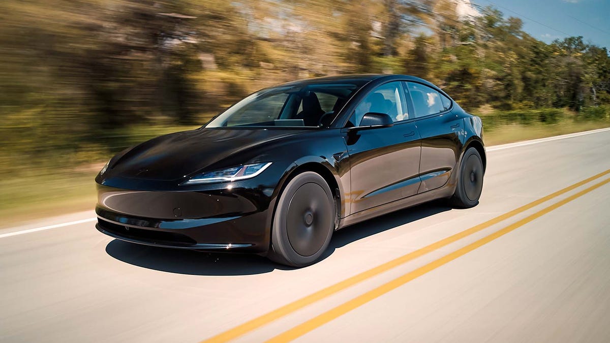 Une Tesla Model 3 Grande Autonomie de couleur bleue, garée devant une borne de recharge futuriste au coucher du soleil, avec une ville moderne en arrière-plan.