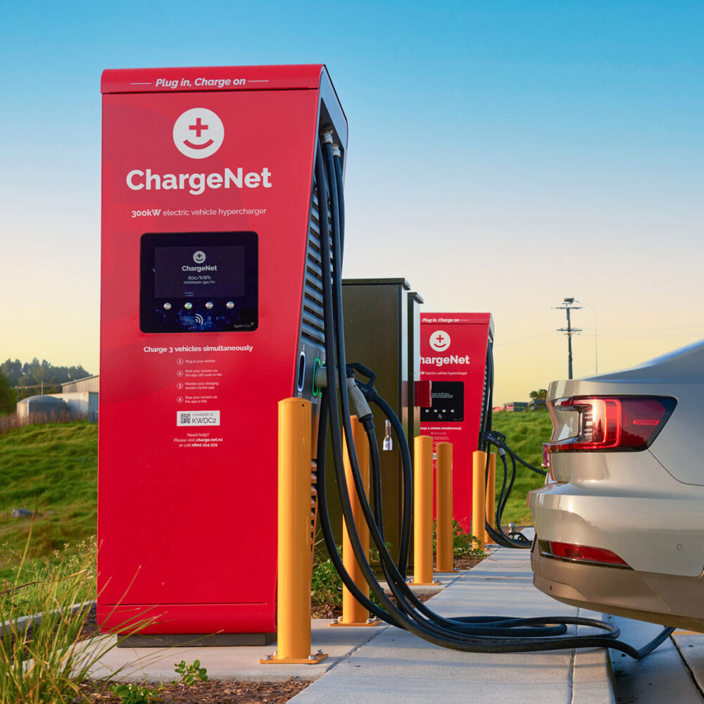 Une voiture électrique en charge à une borne moderne dans un paysage néo-zélandais verdoyant.