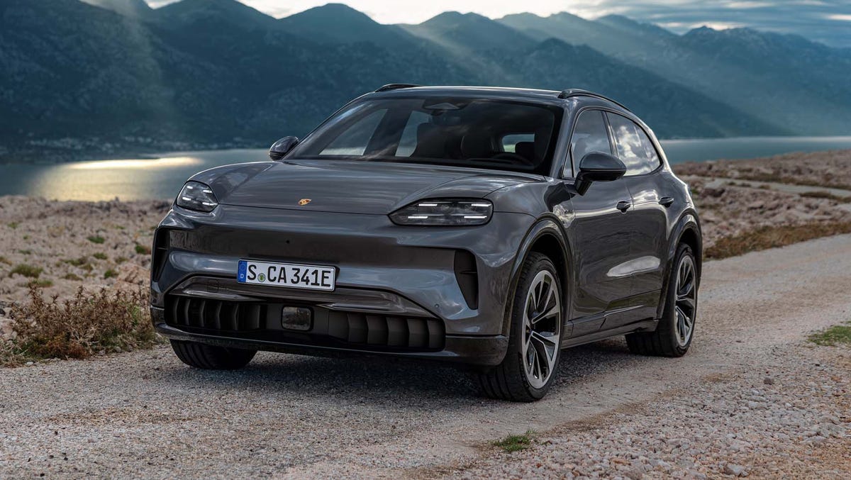 Vue extérieure du Porsche Cayenne S Electric 2026, un SUV électrique de luxe, sur une route de montagne au coucher du soleil.