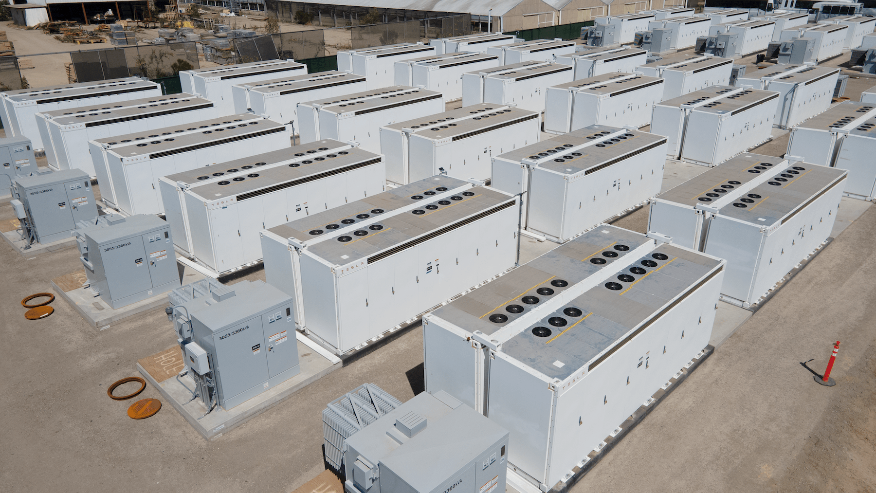 Un Tesla Powerwall fixé sur le mur d'une maison et un grand système Tesla Megapack dans un environnement industriel, tous deux avec des panneaux solaires.