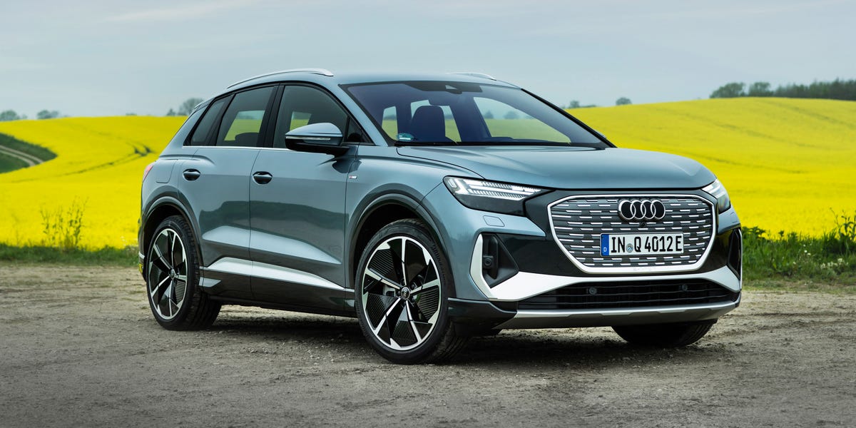 Vue latérale d'une Audi Q4 e-tron Sportback 2026 de couleur foncée roulant sur une route côtière au coucher du soleil.