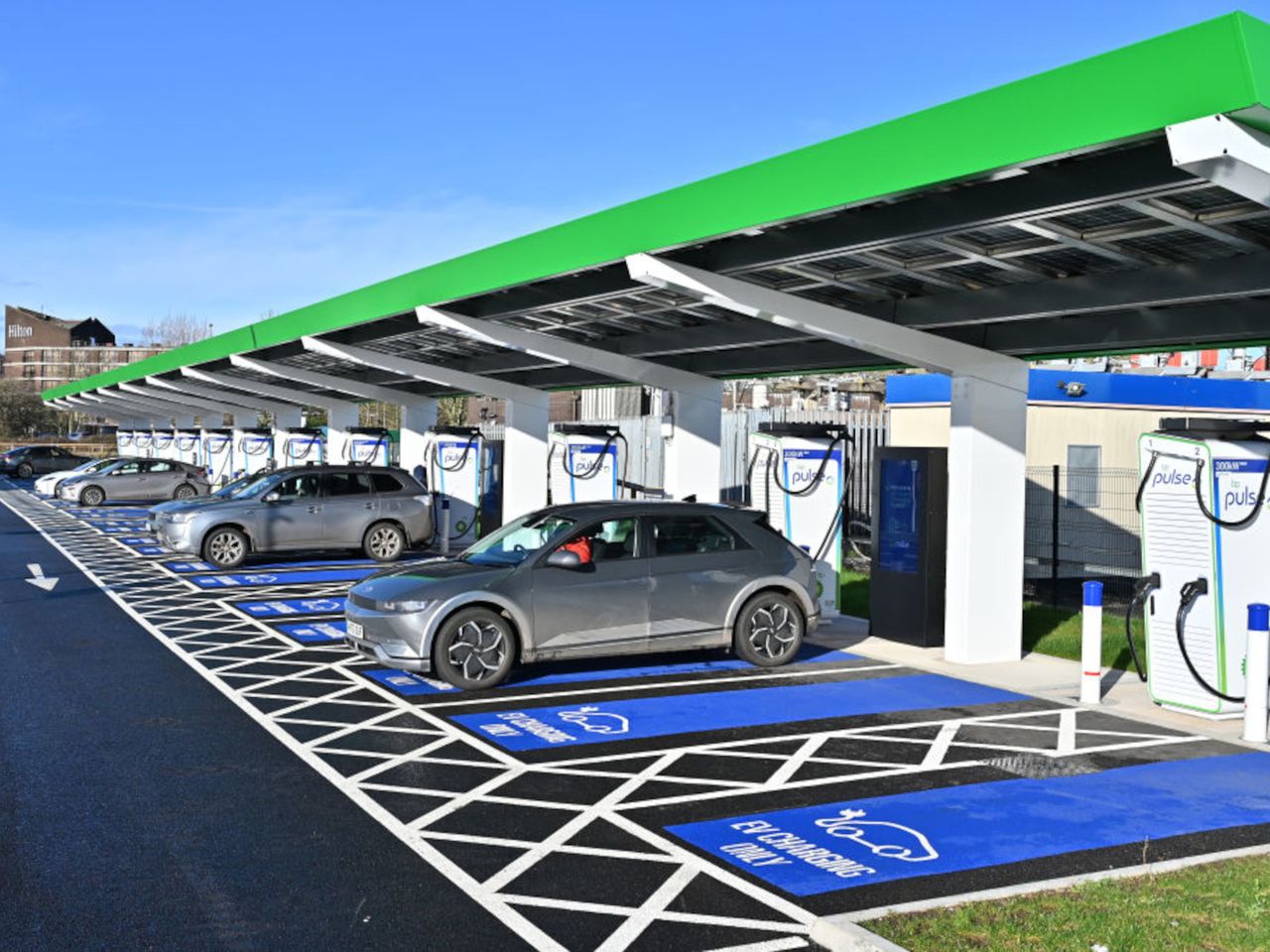 Une voiture électrique blanche en train de charger à une borne de recharge rapide dans une rue urbaine européenne.