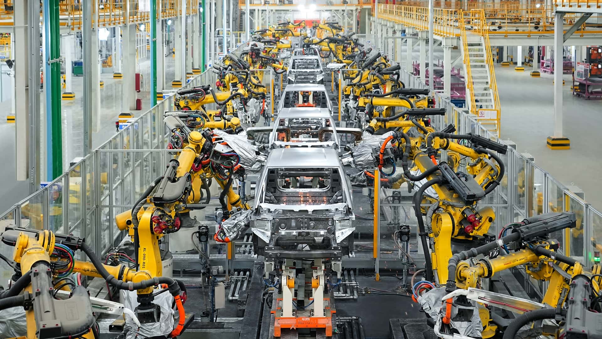 Vue d'ensemble d'une usine de production de voitures électriques BYD en Chine, montrant des robots et des ouvriers assemblant des véhicules sur une chaîne de montage moderne.