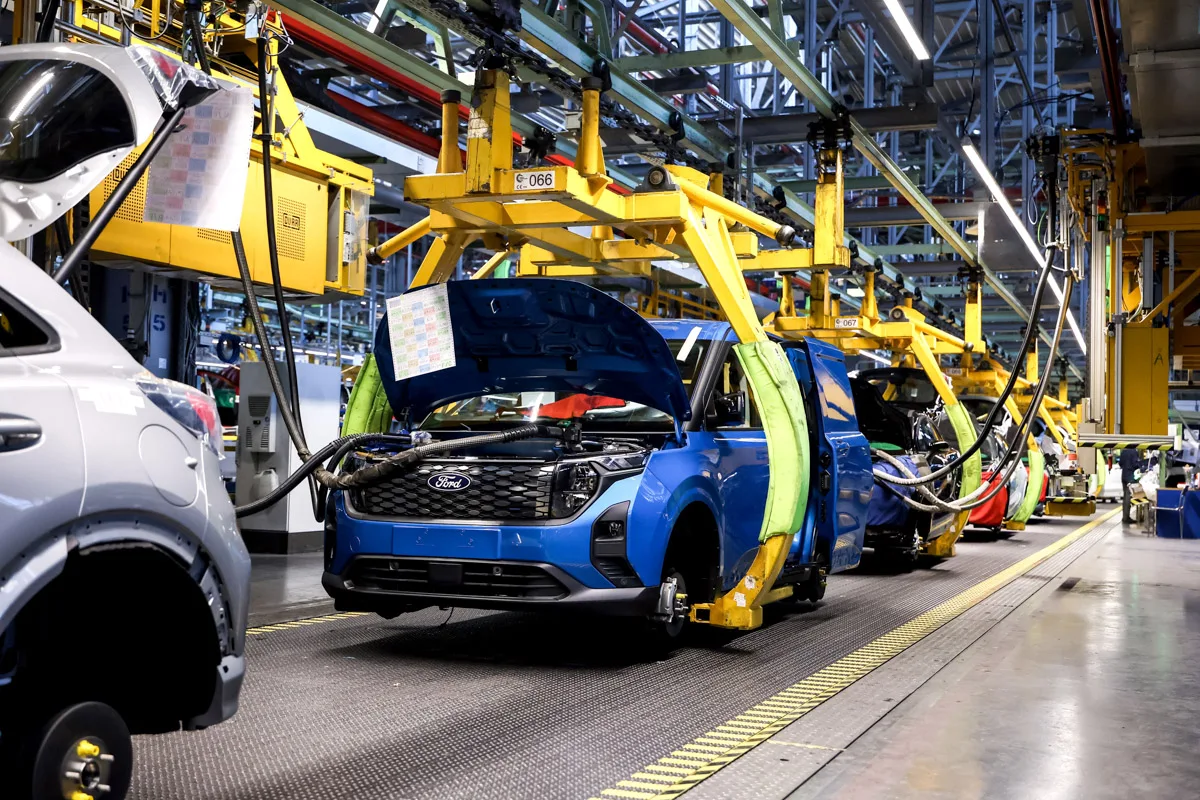 Vue d'ensemble d'une chaîne de montage de véhicules électriques Ford Model e, avec des robots et des techniciens assemblant des voitures.