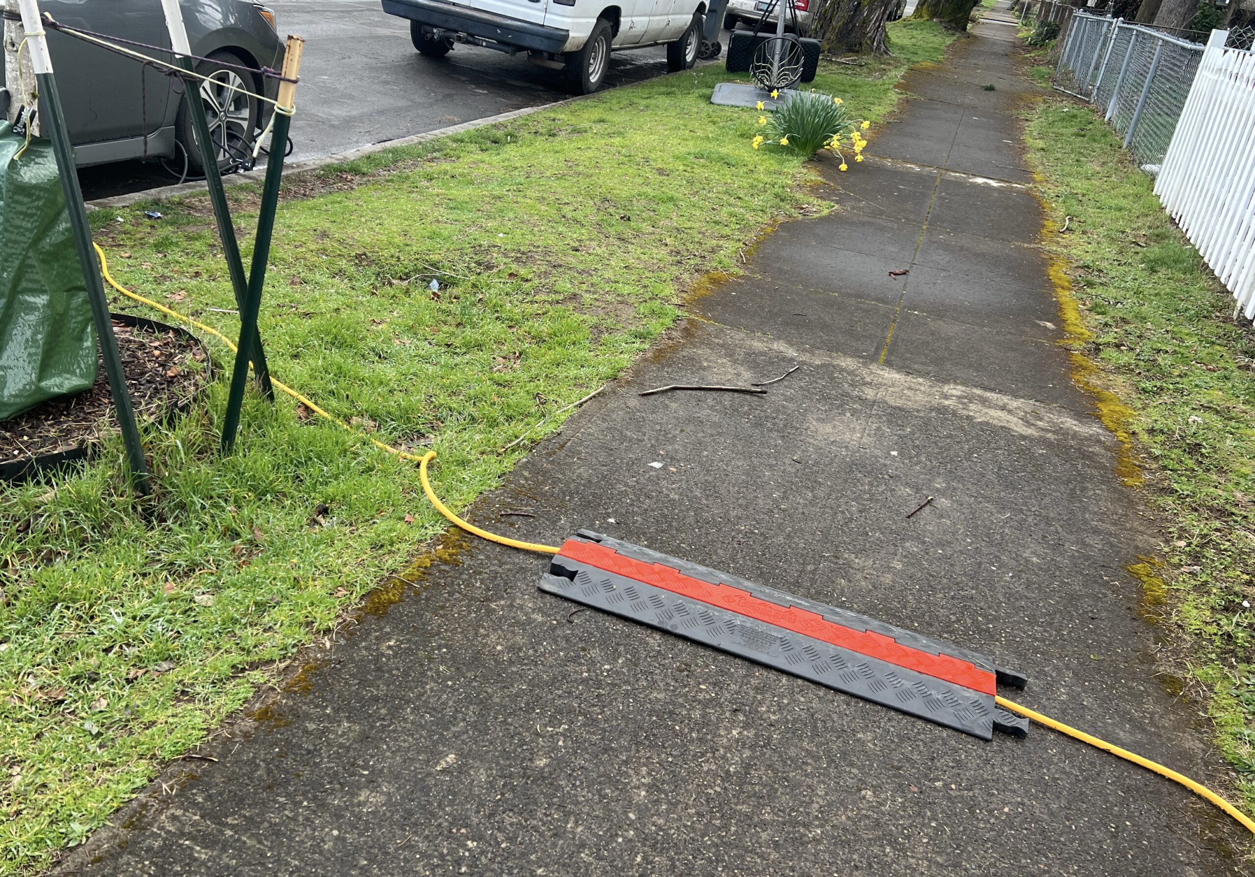 Image rapprochée d'une voiture électrique branchée illégalement à un lampadaire avec une rallonge orange, symbolisant les dangers et l'illégalité de la recharge sauvage.