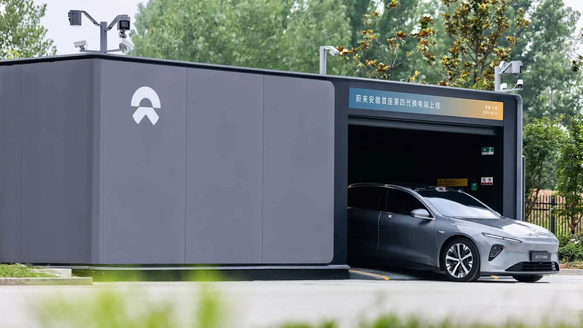 Vue détaillée d'une station d'échange de batteries Nio avec un véhicule électrique en cours de remplacement de batterie par des bras robotiques.