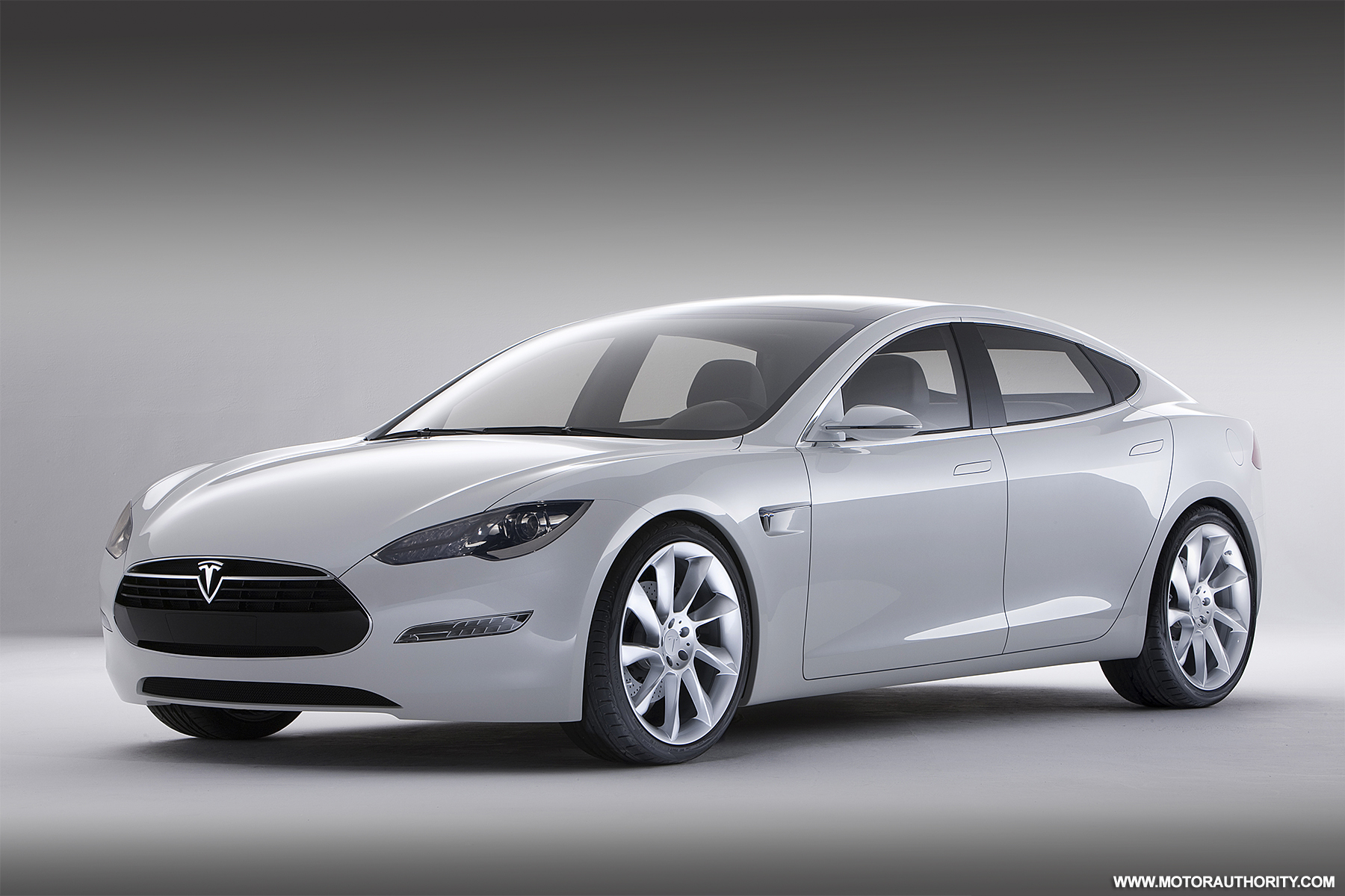 Une Tesla Model S argentée de 2012 en mouvement sur une autoroute au coucher du soleil, mettant en valeur son design élégant.