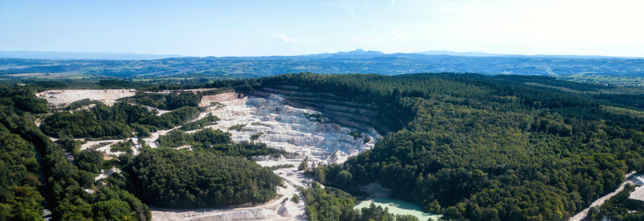 Photographie aérienne d'une mine de lithium à ciel ouvert avec des engins de chantier, située dans un paysage verdoyant.